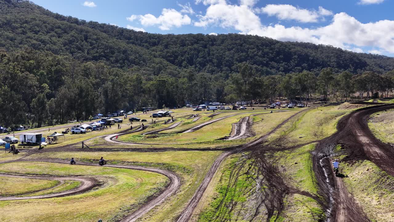 Multiple dirt bikes navigate winding motocross track under bright daylight in scenic rural landscape