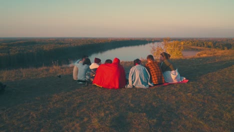 happy-tourists-rest-at-burning-bonfire-on-steep-river-bank