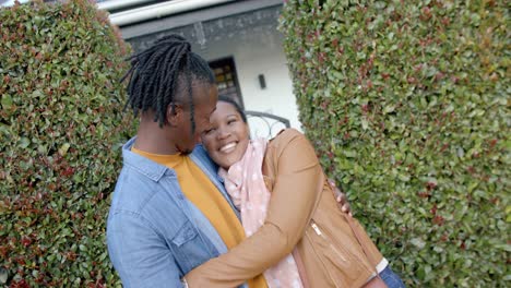 portrait of happy african american couple embracing and standing outside house, slow motion