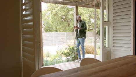 standing on porch, african american man enjoying coffee and looking at garden scenery