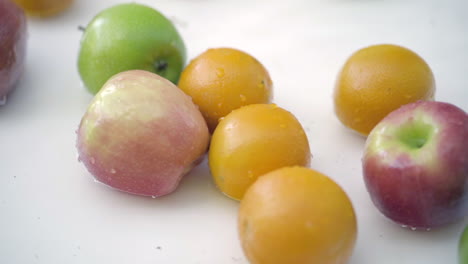 slomo of apples and oranges in water on white backdrop