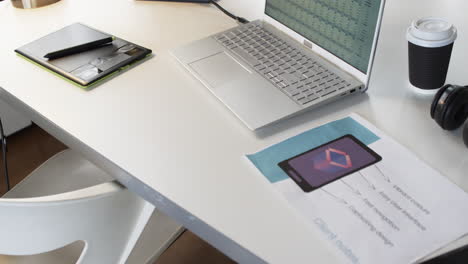 laptop, smartphone, and printed materials are arranged on a desk in a business setting