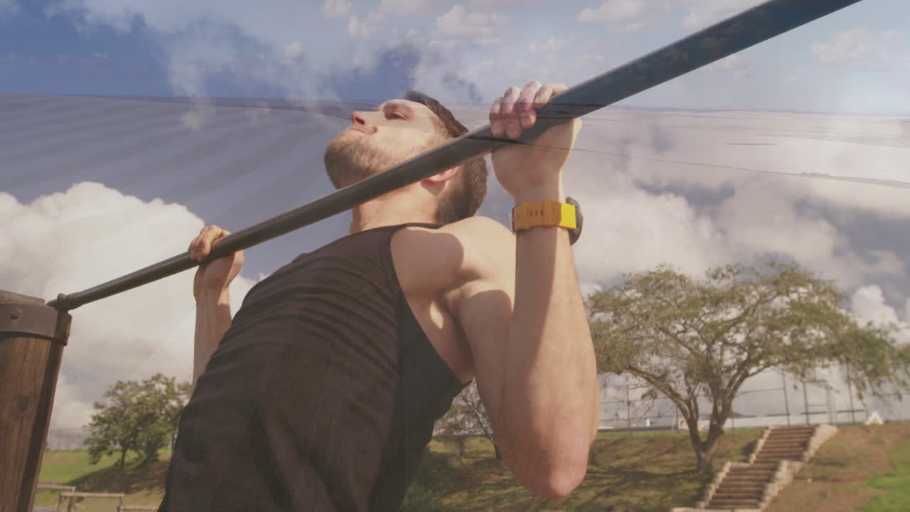 Doing pull-ups outdoors, man in black tank top under cloudy sky