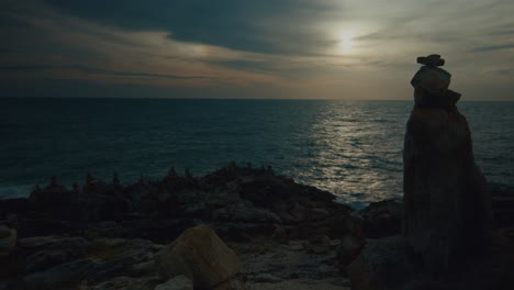 sunset over the ocean with stone cairns