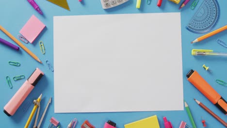 video of school supplies, notebook, pens, marker pen and white sheet of paper over blue background