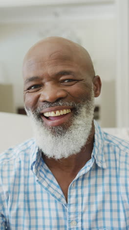 retrato de video vertical de un hombre afroamericano de edad avanzada feliz con barba sonriendo en la sala de estar
