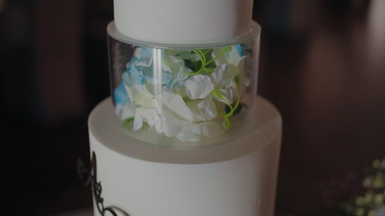 Close-up of a unique white tiered cake featuring a transparent section filled with delicate blue and white flowers