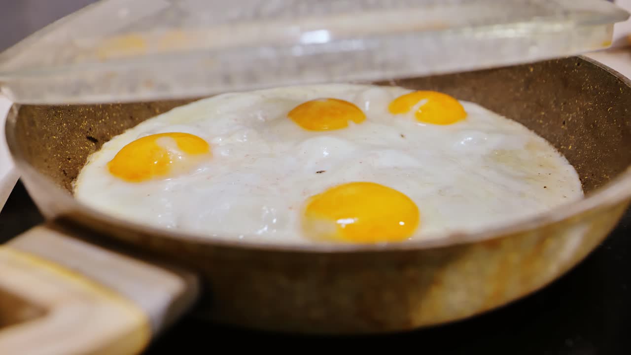 Close up telur yang digoreng dengan putih telur yang bergelembung, uap di bawah tutup kaca dapur rumah