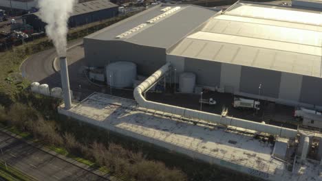 aerial shot of smoking chimney on factory moving to the right with lorries hauling cargo