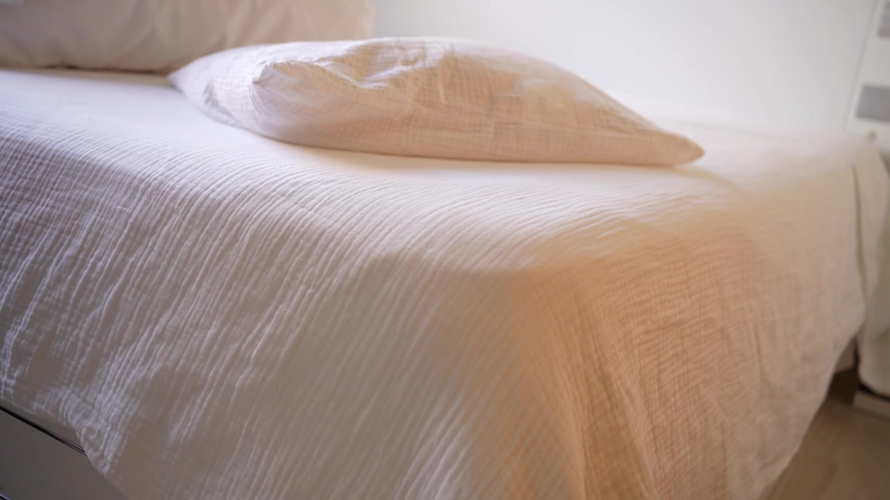 Seprai putih yang nyaman terhampar di atas tempat tidur yang nyaman di oasis kamar tidur yang indah