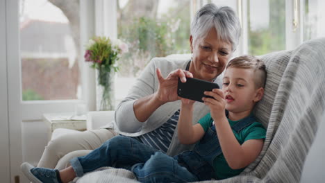 Fröhlicher-Kleiner-Junge,-Der-Sein-Smartphone-Benutzt-Und-Großmutter-Zeigt,-Wie-Man-Ein-Mobiltelefon-Benutzt,-Und-Oma-Moderne-Technologie-Beibringt,-Intelligentes-Kind,-Das-Oma-Zu-Hause-Hilft,-4k