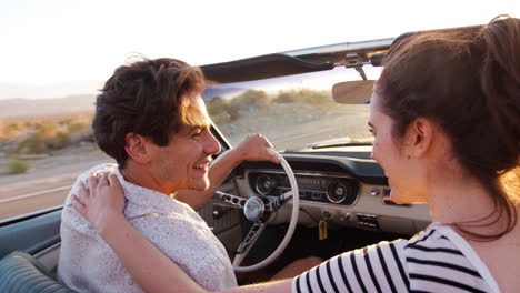 una joven pareja blanca conduciendo un coche abierto, vista trasera, de cerca.