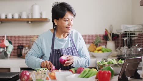 asian senior woman using digital tablet while removing onions skin in the kitchen at home