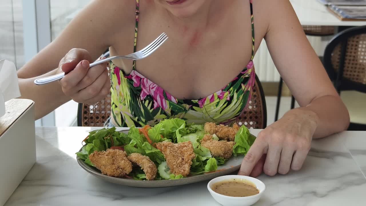 Mulher comendo uma salada de frango em um restaurante