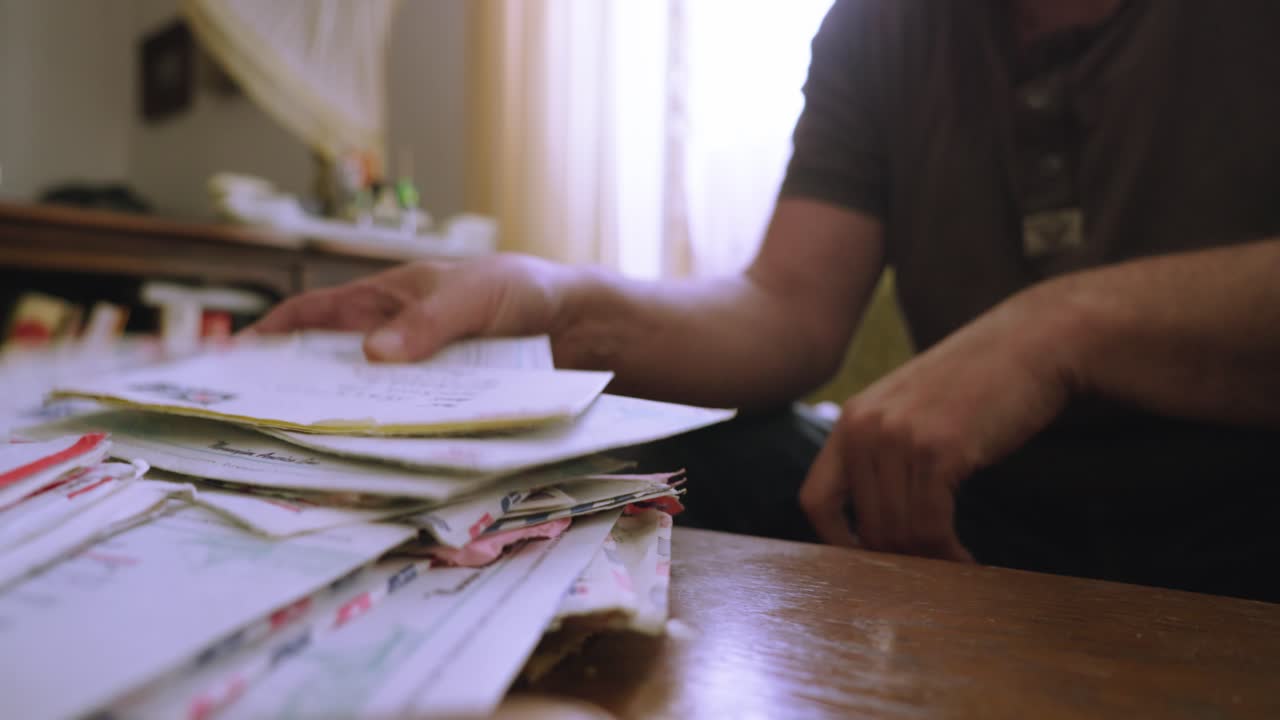 A person's hands search for a letter in a pile of correspondence made up of letters and envelopes
