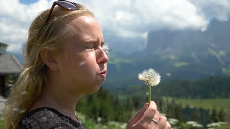 blonde female model blowing a dandelion flower in the wind the wrong way in the val gardena area, dolomites italy