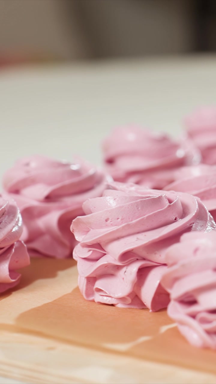 Primo piano di biscotti meringa rosa a spirale disposti. La texture lucida e il motivo a spirale sono evidenziati da una luce soffusa. Lo sfondo rimane sfocato mantenendo l'attenzione esclusivamente
