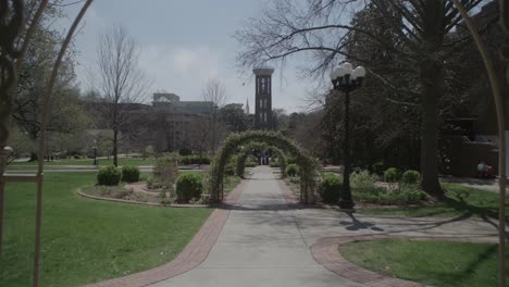 un disparo medio a través de un mirador ornamentado hacia un camino alineado con arcos y una torre alta y estrecha en la distancia en nashville, rodeado de exuberante vegetación y un cielo despejado