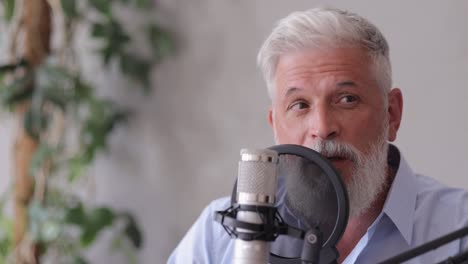 man records a podcast or interview with a microphone in a recording studio. senior sound engineer or radio host. an adult gray-haired man creates audio content