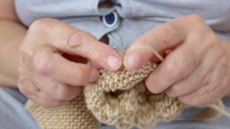 close-up of an old woman's hand with wrinkles and cracks knitting warm clothes for her family. hobby closeup knitting by grandmother. favorite pastime of retirees