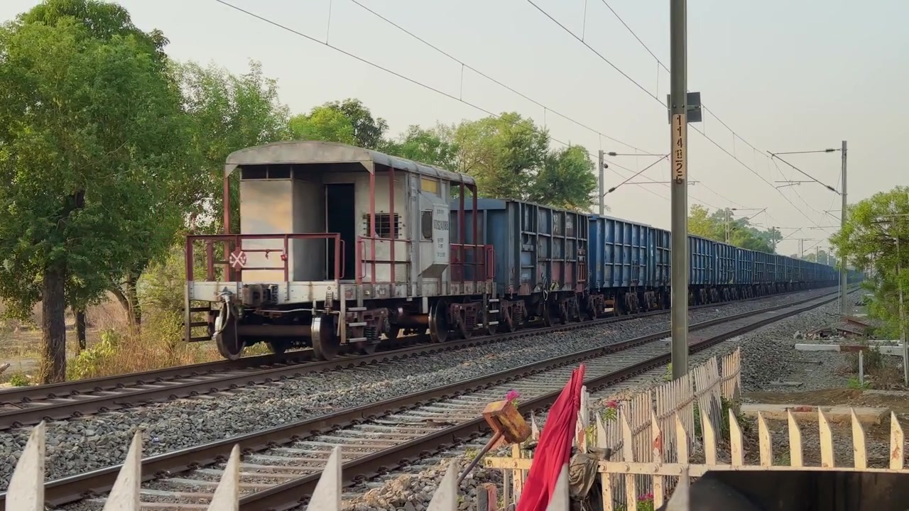 Lungo treno merci che si muove lungo un corridoio ferroviario elettrificato con vagoni merci che si estendono in lontananza, evidenziando la logistica dei trasporti