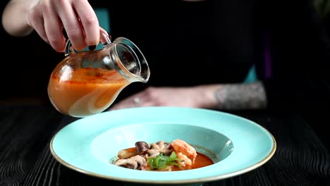 el chef vierte sopa de tom yum sobre un plato de mariscos