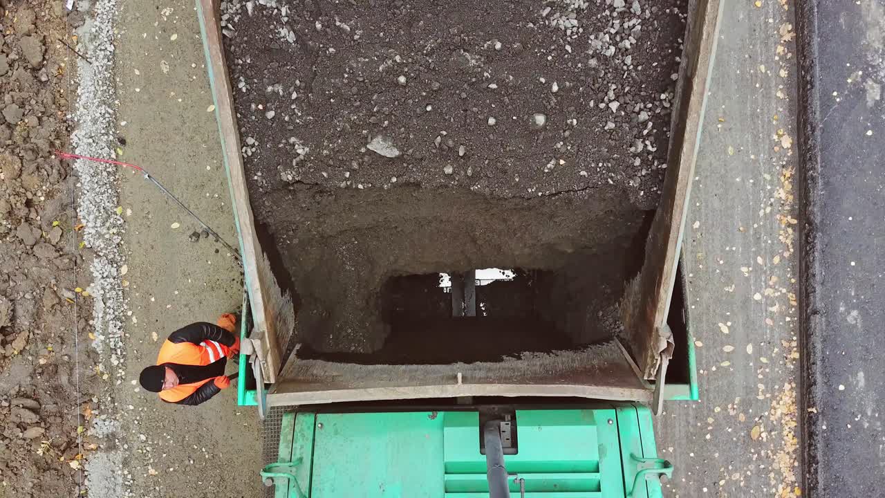 Vista dall'alto di un camion per l'asfaltatura all'aperto. Veduta aerea di bitume nero che viene versato dalla macchina sulla strada. Processo di asfaltatura.
