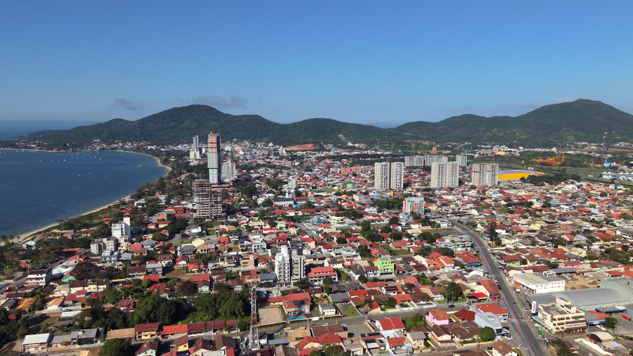 Aerial clip gliding over city with houses and buildings on a calm sunny afternoon. Hills in background