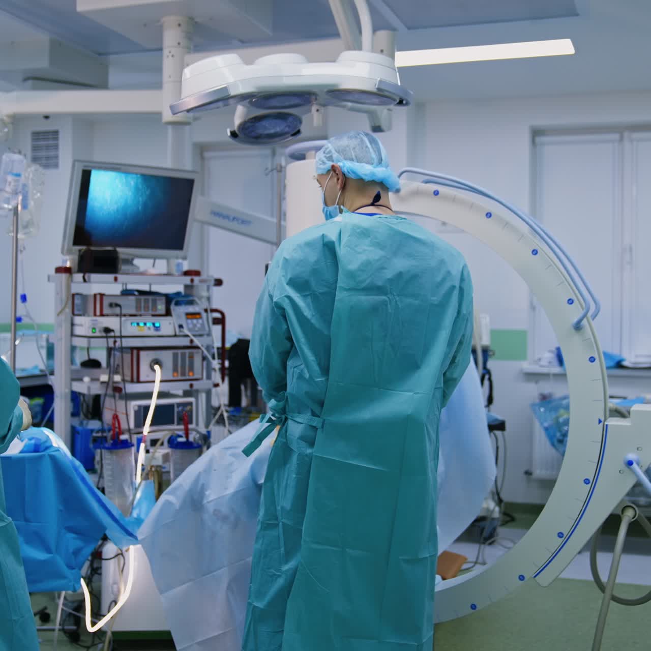 Medic in x-ray protection outfit takes C-arm machine away from a patient. Surgical operation in modern operational room