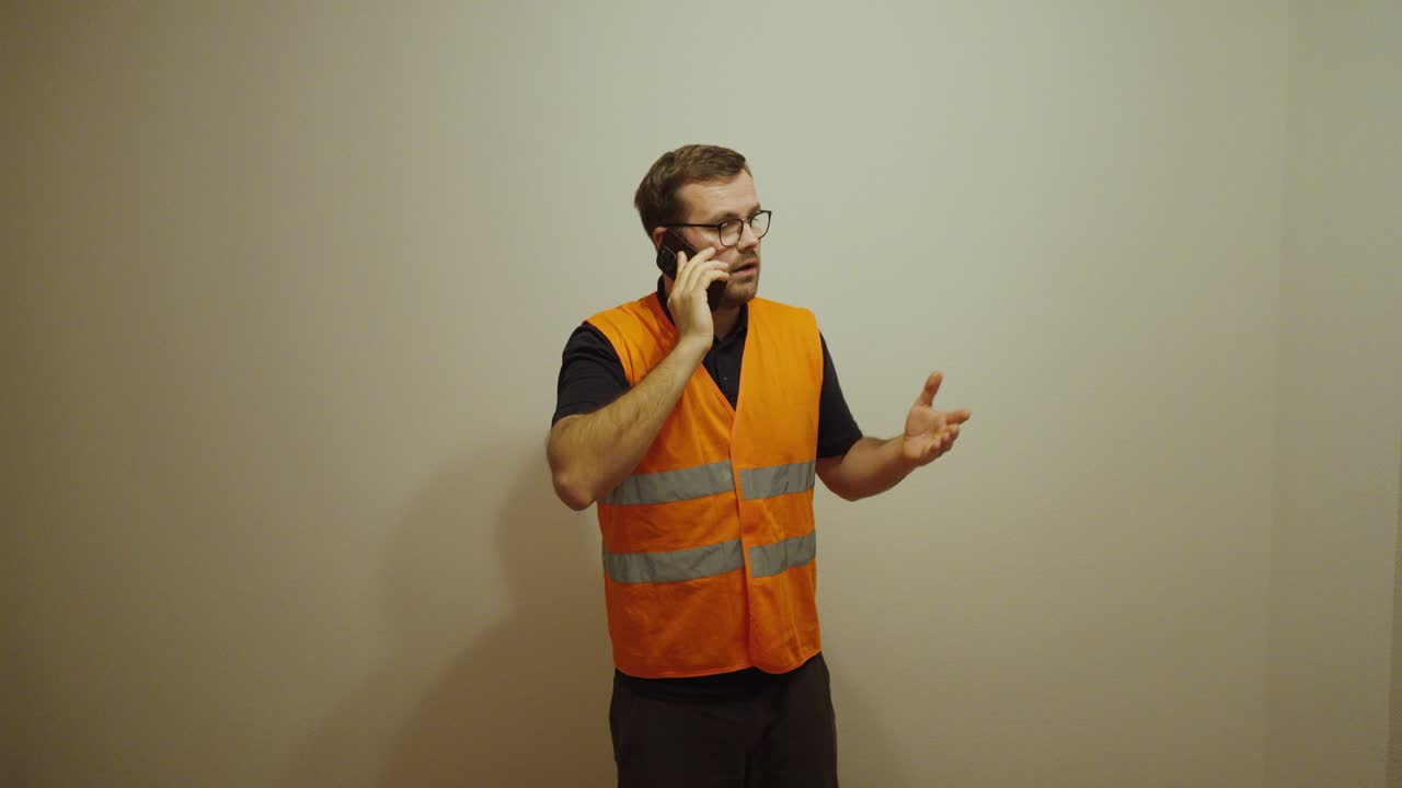 A man wearing a reflective safety vest talks on the phone. Concept of communication, construction site, safety, coordination, and teamwork at work