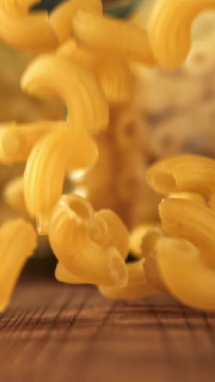 Maccheroni dorati che cadono su una superficie di legno al rallentatore