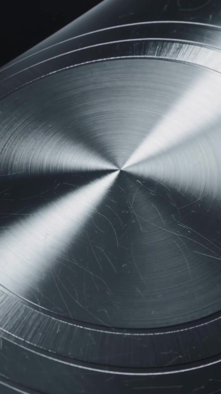 Video verticale: Disco metallico rotante che segue il cambiamento di luce in macro studio, rivelando gli anelli.