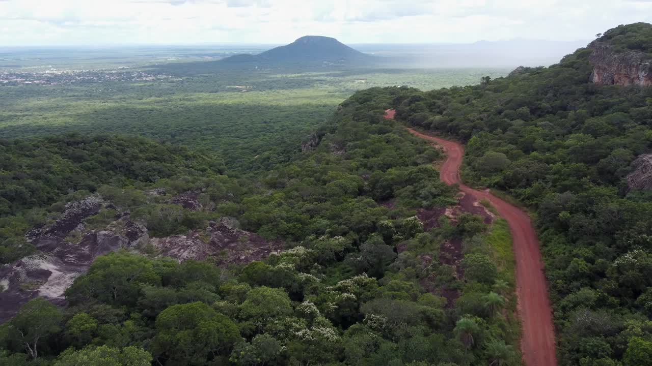 Flyover rough red dirt road on forested escarpment plateau in Bolivia