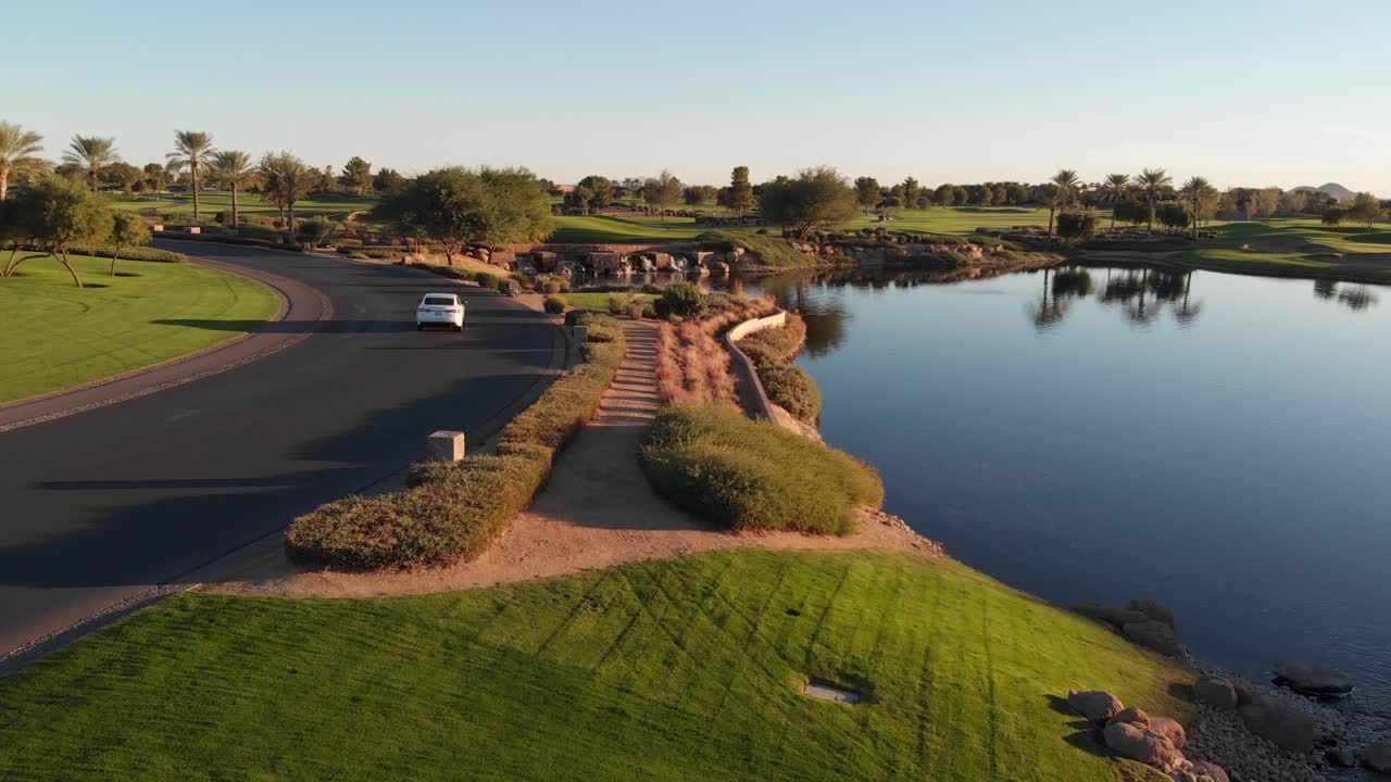 Drone footage from a golf course near a residential neighborhood in Arizona. Shot of the water hazard and roadway near the course.