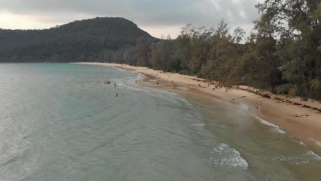 Tourists-enjoying-the-warm-water-of-Lazy-beach-during-a-cloudy-evening---Aerial-Fly-over-shot