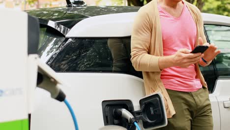 hombre usando teléfono móvil mientras carga un coche eléctrico 4k