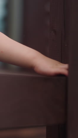 Toddler boy in blue t-shirt touches wet wooden beam of handrail walking along veranda deck at cottage house extreme closeup slow motion