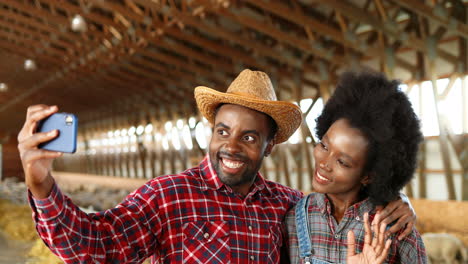 mujer y hombre afroamericanos granjeros con traje de mezclilla haciendo un selfie con teléfono inteligente en un establo