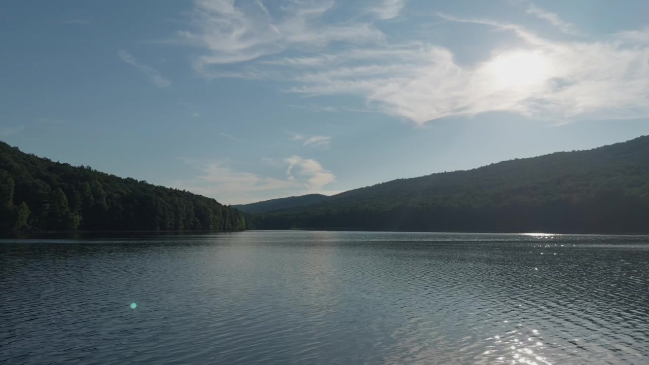 Vue sur un plan d'eau serein reflétant le ciel couvert, avec des rives luxuriantes et boisées à l'arrière-plan