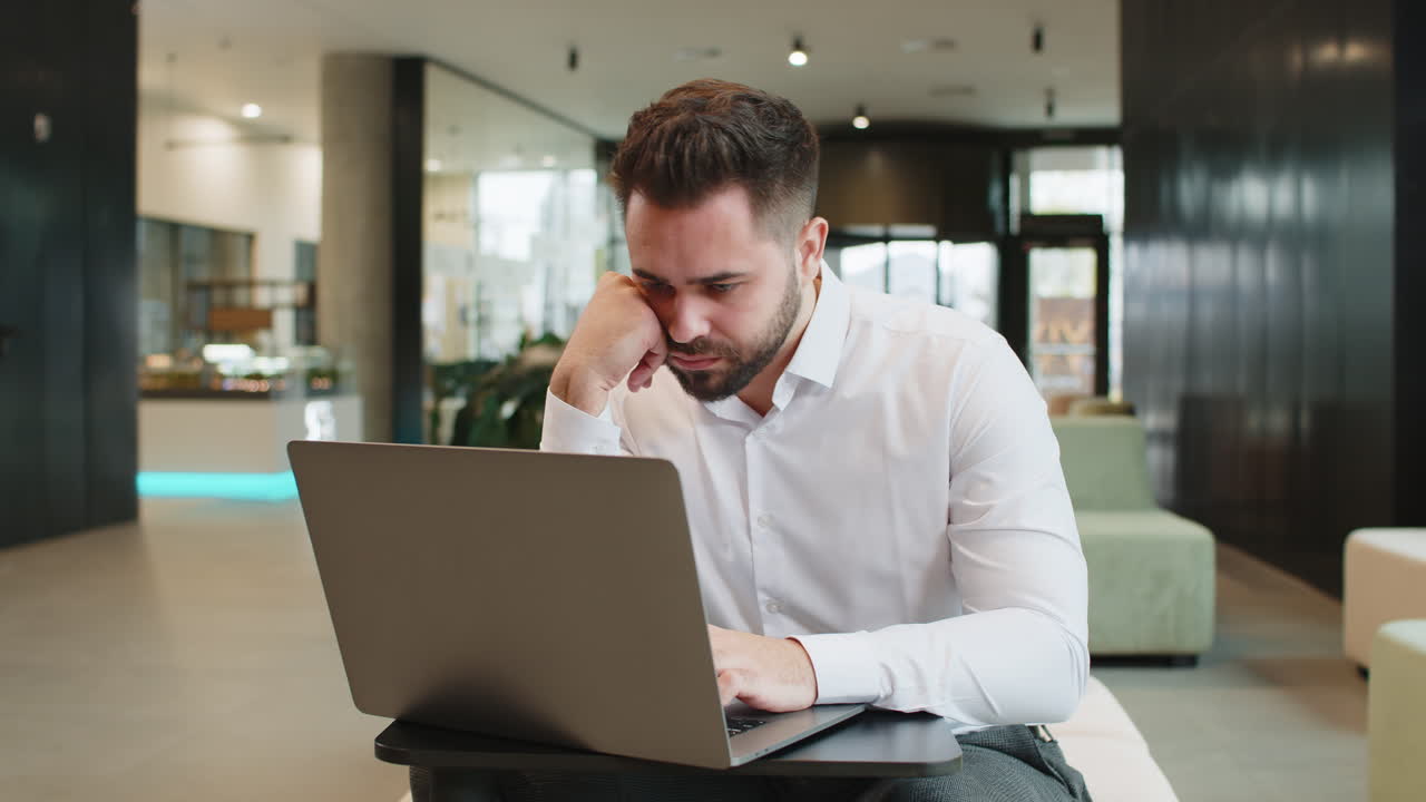 joven hombre de negocios cansado y enfermo usando una computadora portátil que sufre de dolor de cabeza problema de tensión en el vestíbulo del hotel