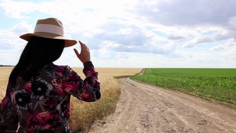 girl in dress and hat walking on dirt road through fields - medium shot