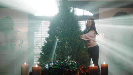 Woman Decorating a Christmas Tree in a Room with Atmospheric Lighting