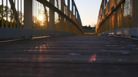 sol brillando a través de los rieles metálicos de un puente peatonal de madera durante la puesta de sol