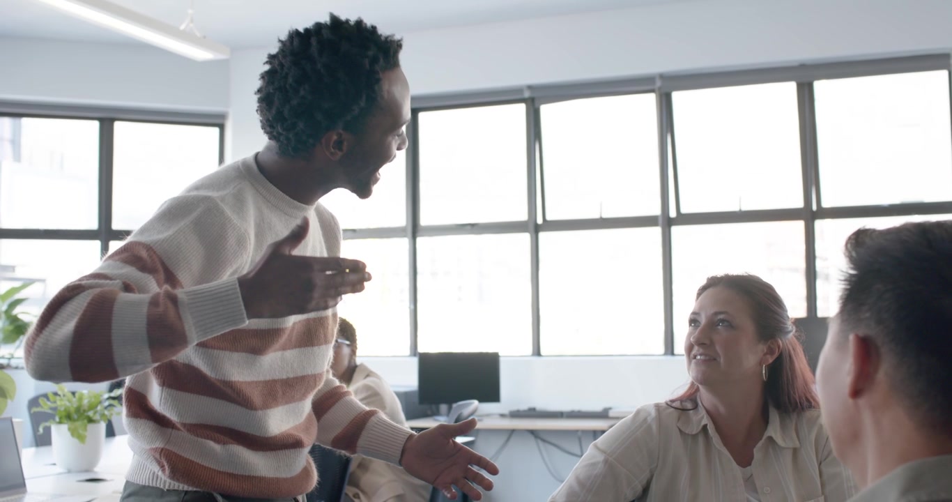 Diverse team seeing African American man approaching, explaining idea in striped sweater in office
