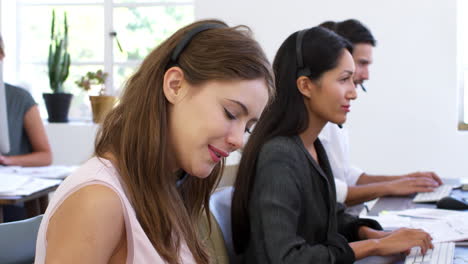 white woman in headset smiles to camera in open plan office