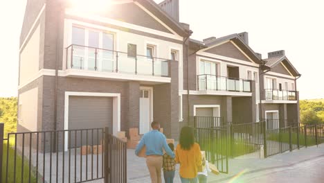 rear view of african american family with small children walking and moving in new home at suburb