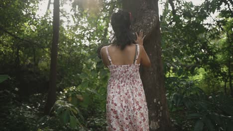 a beautiful indian girl moving her palm on a tree stem's surface in a day time