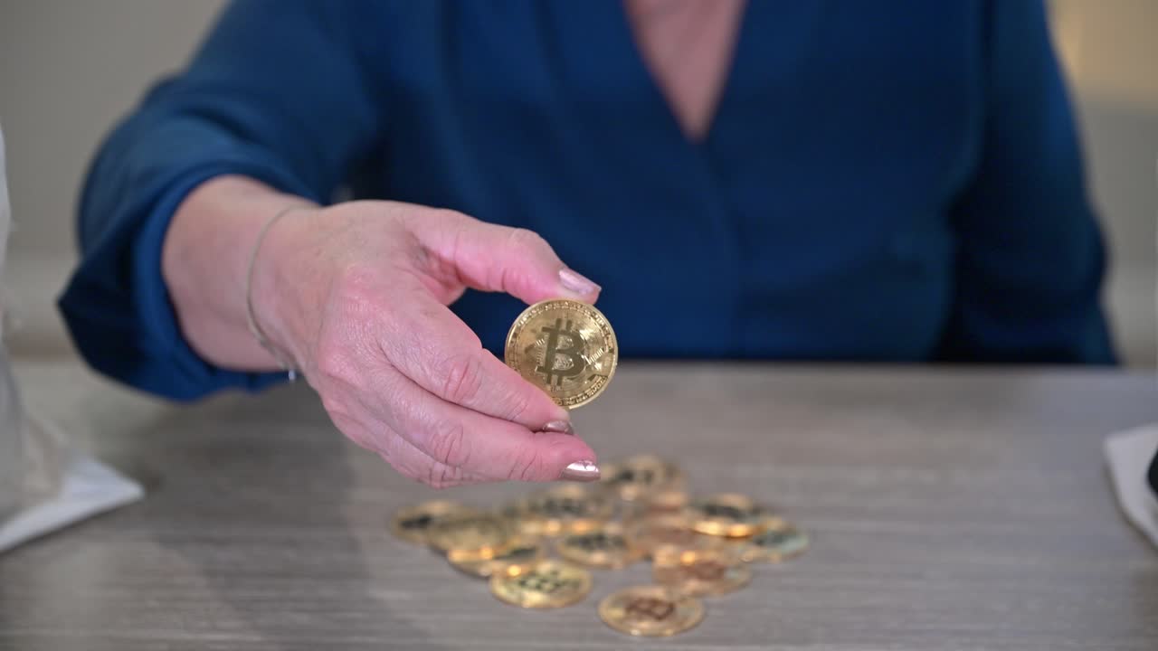 mano de mujer anciana sosteniendo un token de bitcoin que agarró de una pila de monedas