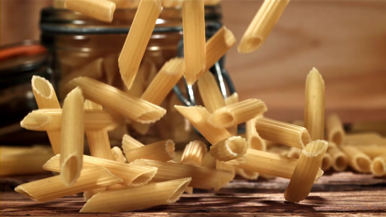Penne che cadono al rallentatore su un tavolo di legno rustico.