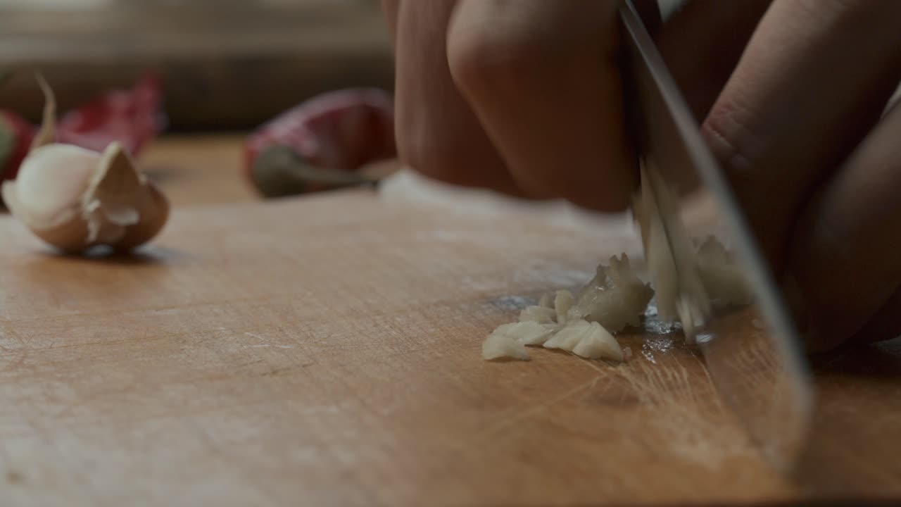 Hands Chopping Garlic on Wooden Cutting Board